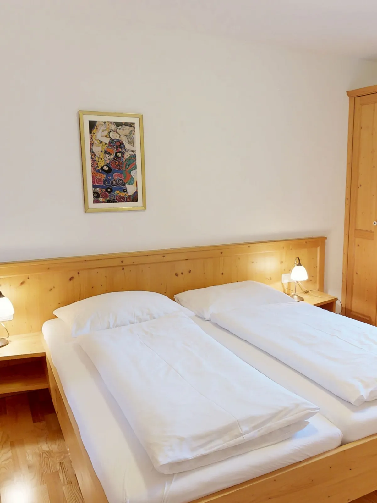 Blick in ein Schlafzimmer mit zwei Betten, Nachttischlampen und einem Gemälde.