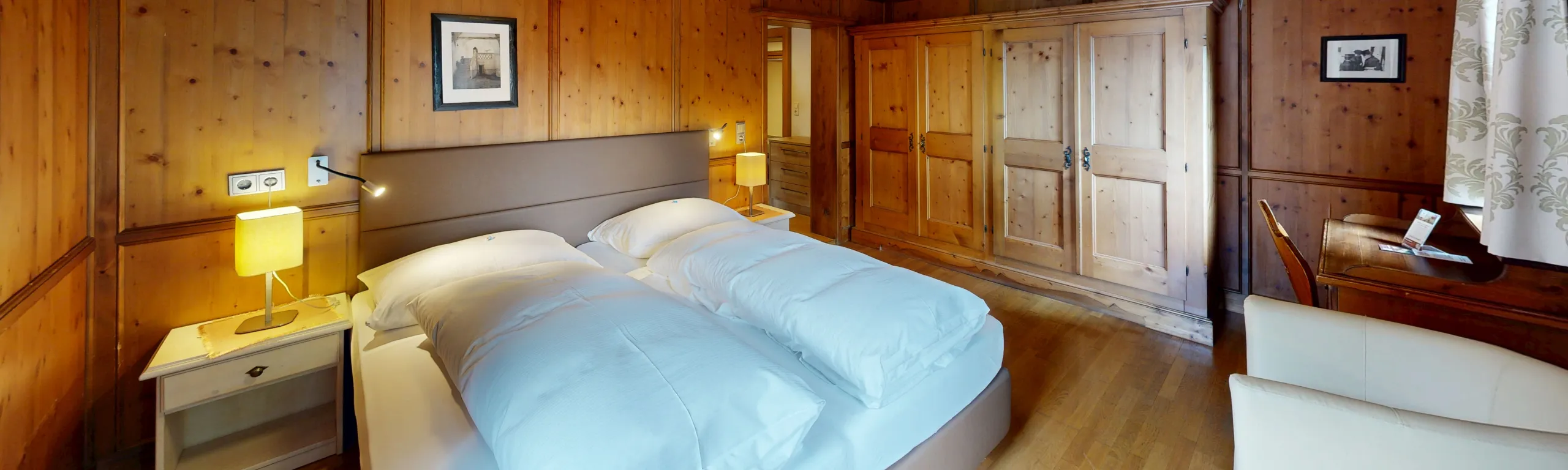Helle, gemütliche Hotelzimmer mit Holzwänden, Bett und Nachtischlampe.
