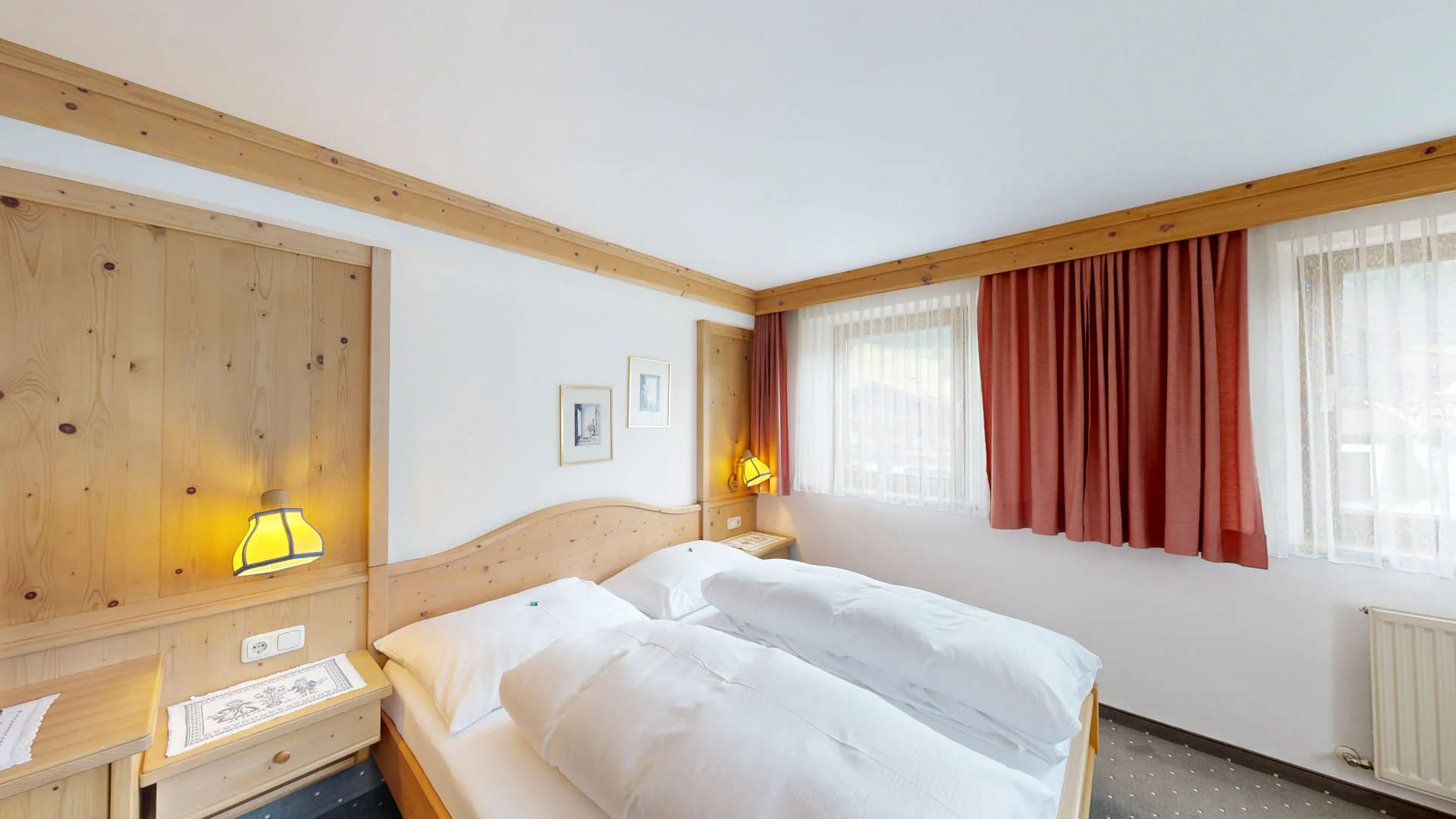 Helles Hotelzimmer mit Holzpaneelen, roten Vorhängen und Doppelbetten.