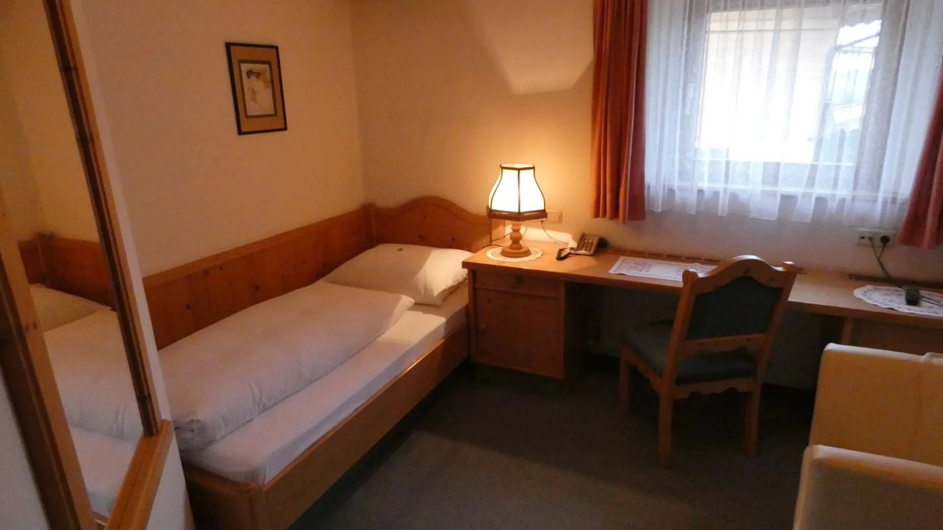 Gemütliches Einbettzimmer mit Bett, Schreibtisch und Tischlampe