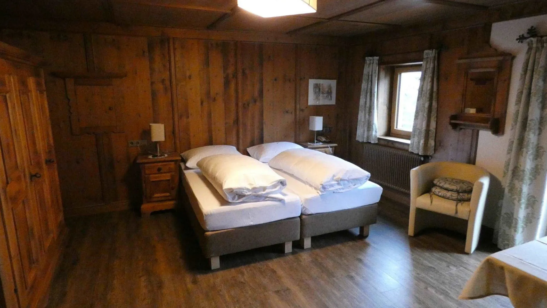 Holzvertäfeltes Zimmer mit zwei Betten, Stuhl und Fenster in Ellmau