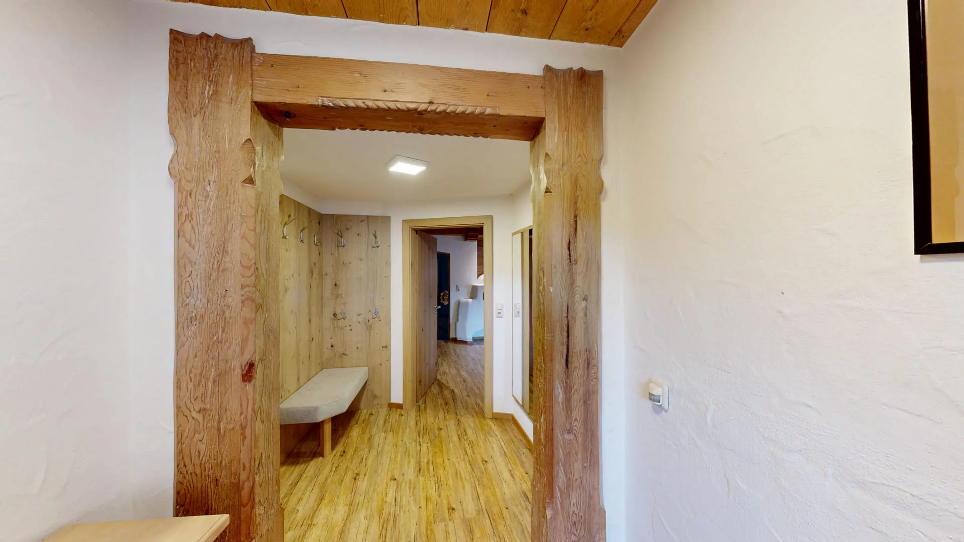 Heller Flur mit Holzboden und Wänden, Blick durch einen offenen Türrahmen
