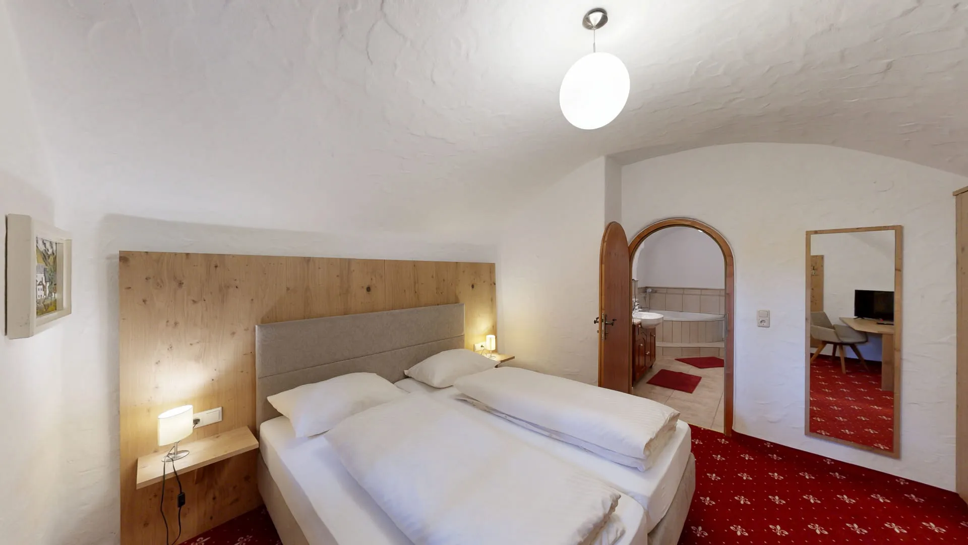 Helle Hotelzimmer mit Doppelbett, rotem Teppich und schlichten Möbeln.