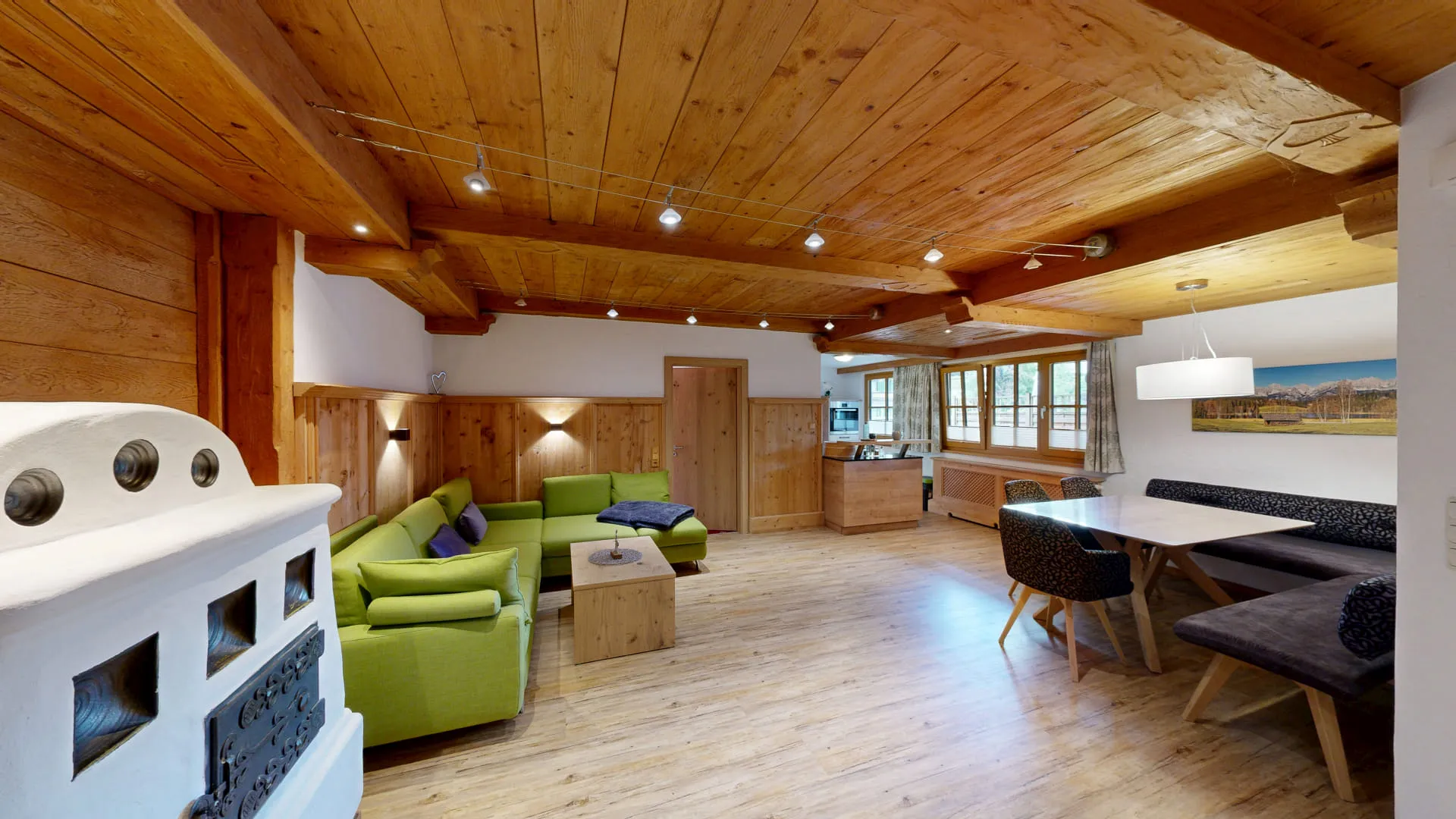 Geräumiger Wohnraum mit Holzdecke, grünen Sofas und Esstisch.